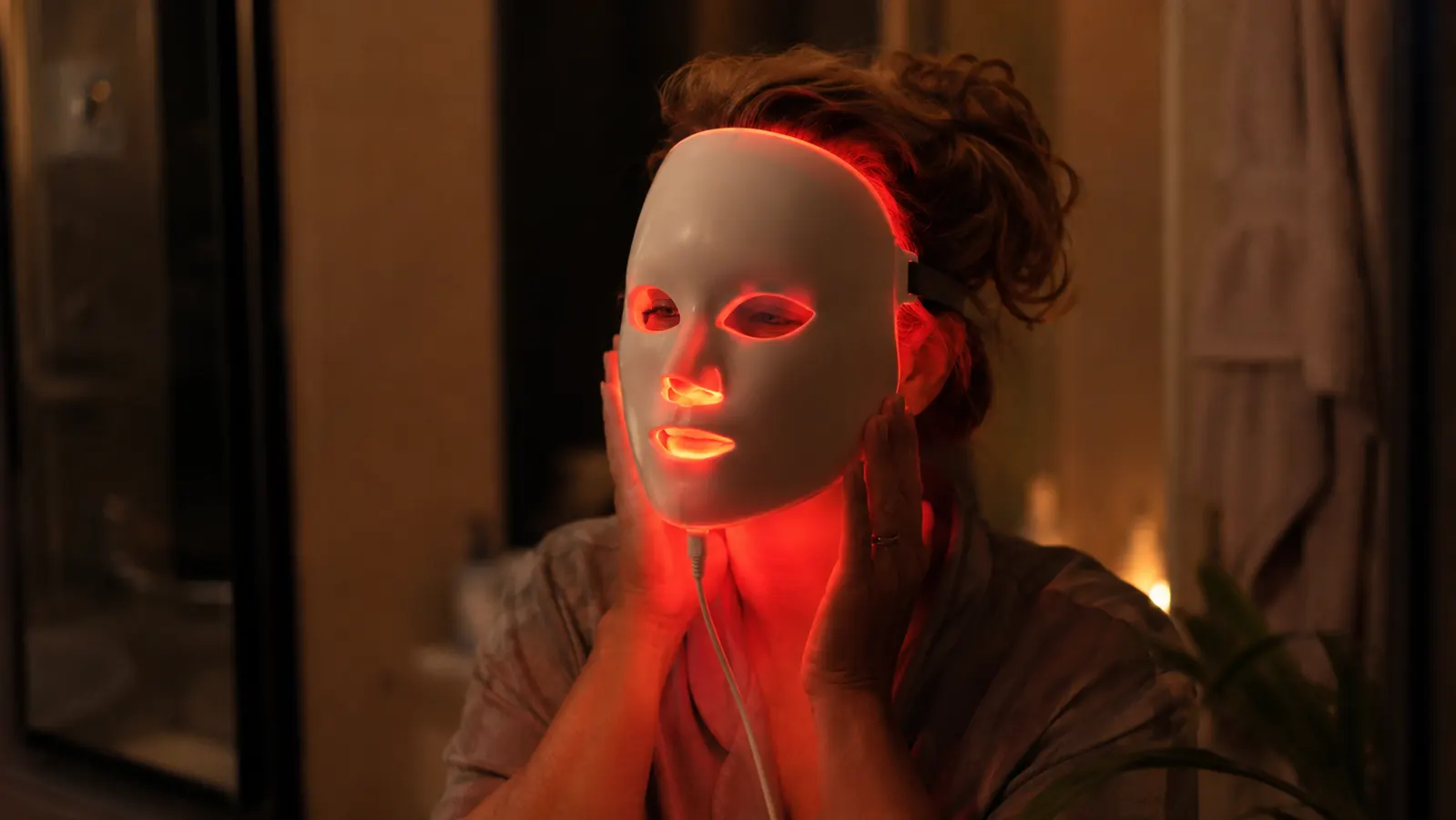 Woman wearing the NVBOTY red light therapy mask at her bathroom counter in the evening