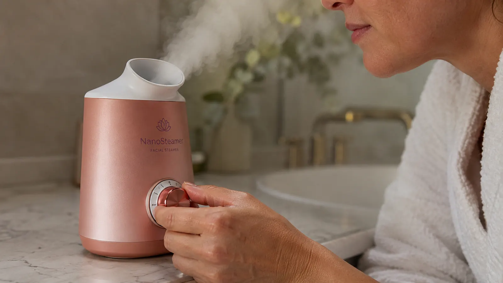 Hand adjusting the temperature dial on the NanoSteamer while a face rests in the steam