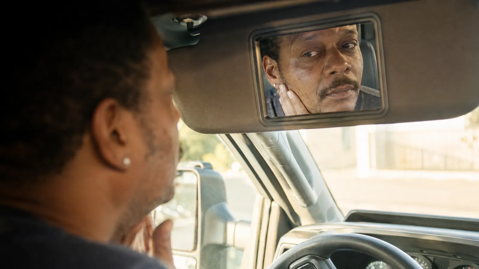 A person looking at calmer, less flaky skin in a small mirror inside a truck cab